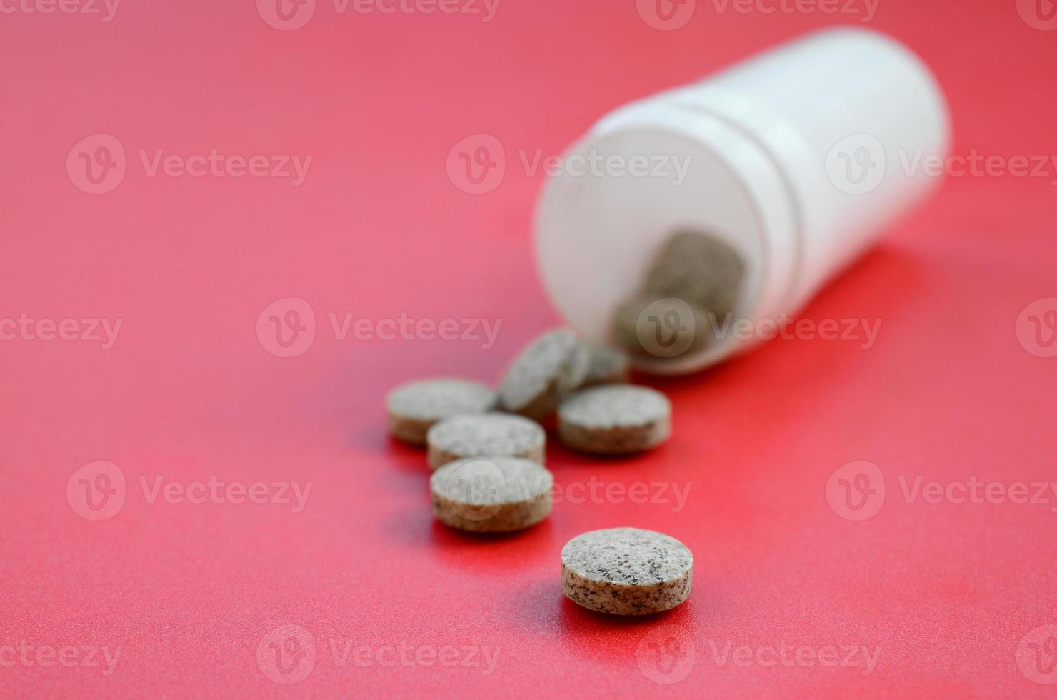 mehrere braune tabletten fallen auf der roten oberfläche aus dem plastikglas. Hintergrundbild zu medizinischen und pharmazeutischen Themen foto