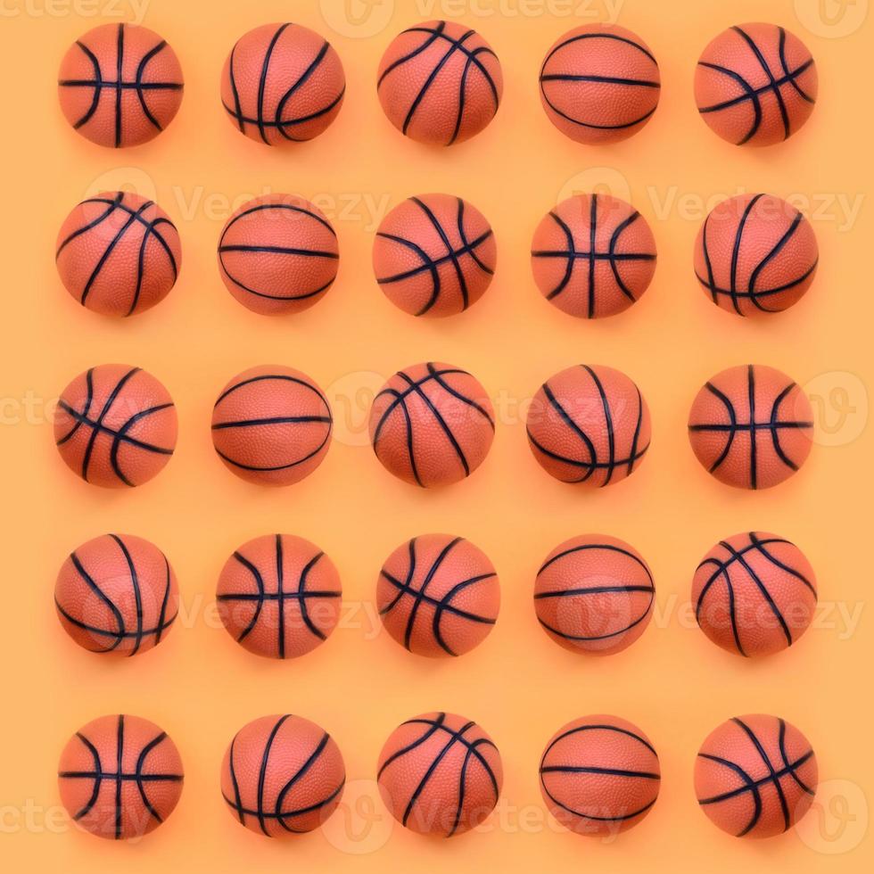 Viele kleine orangefarbene Bälle für Basketball-Sportspiele liegen auf Texturhintergrund aus modepastellorangefarbenem Papier in minimalem Konzept foto