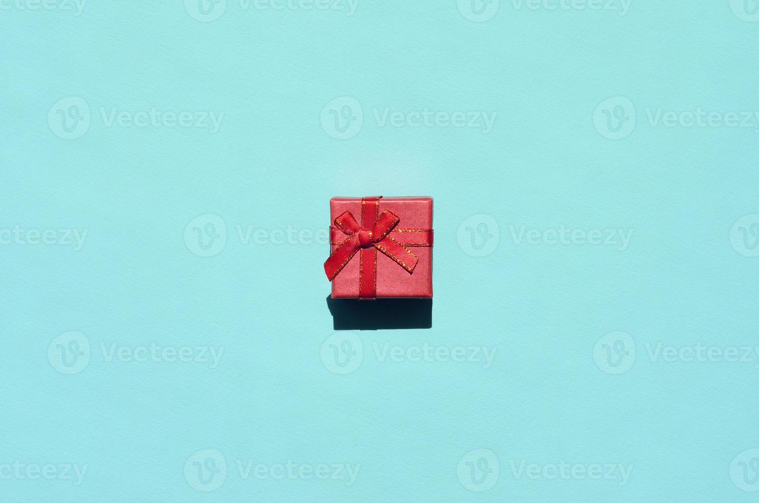 kleine rot-rosa geschenkbox liegt auf texturhintergrund von mode trendigem pastellblauem farbpapier in minimalem konzept foto