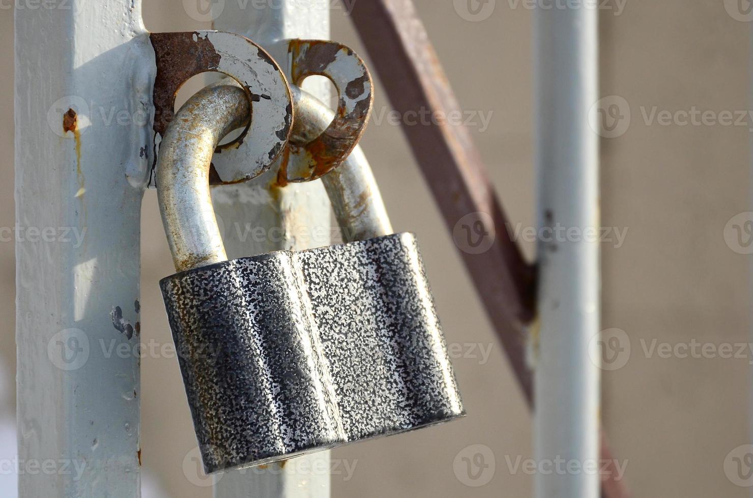 An einem Metalltor hängt ein großes graues Vorhängeschloss foto