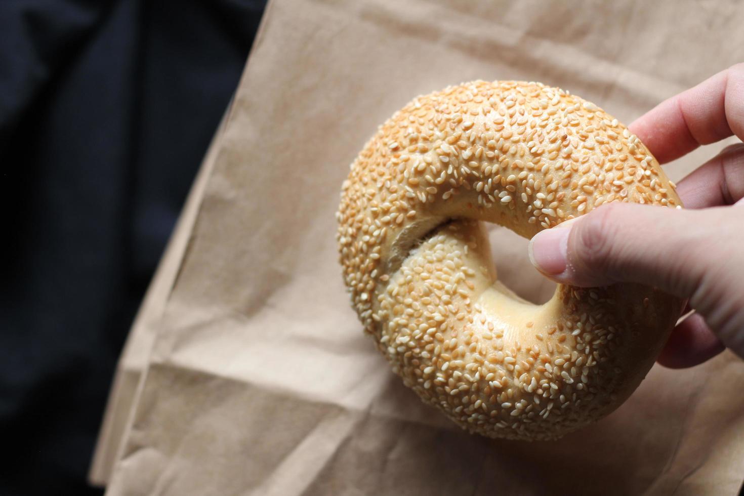 Die Hand eines Mannes hält einen Bagel auf einer braunen Papiertüte. foto