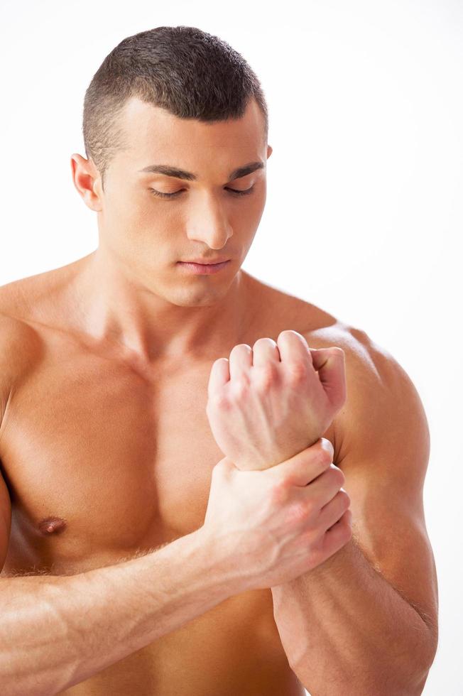 Schmerzen im Handgelenk fühlen. hübscher junger muskulöser Mann, der sein Handgelenk berührt, während er vor weißem Hintergrund steht foto