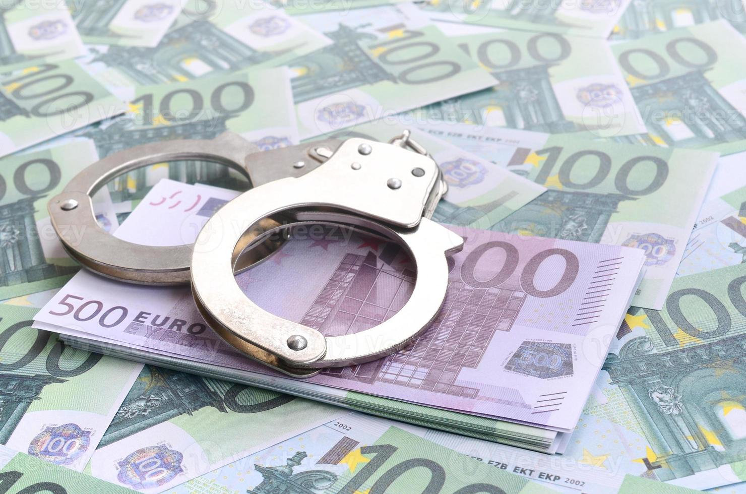 Polizeihandschellen liegen auf einem Satz grüner Geldscheine von 100 Euro. viel Geld bildet einen unendlichen Haufen foto