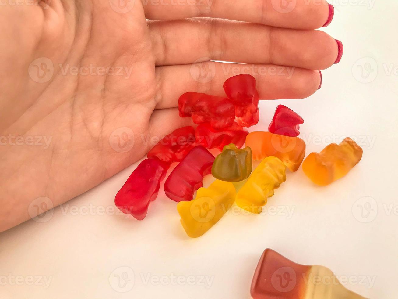 Gummibonbons auf einem rosa matten Hintergrund. Jujube schließt Mädchen mit roter Maniküre. Süßigkeiten zwischen Kindern teilen. faires Teilen des Nachtischs foto