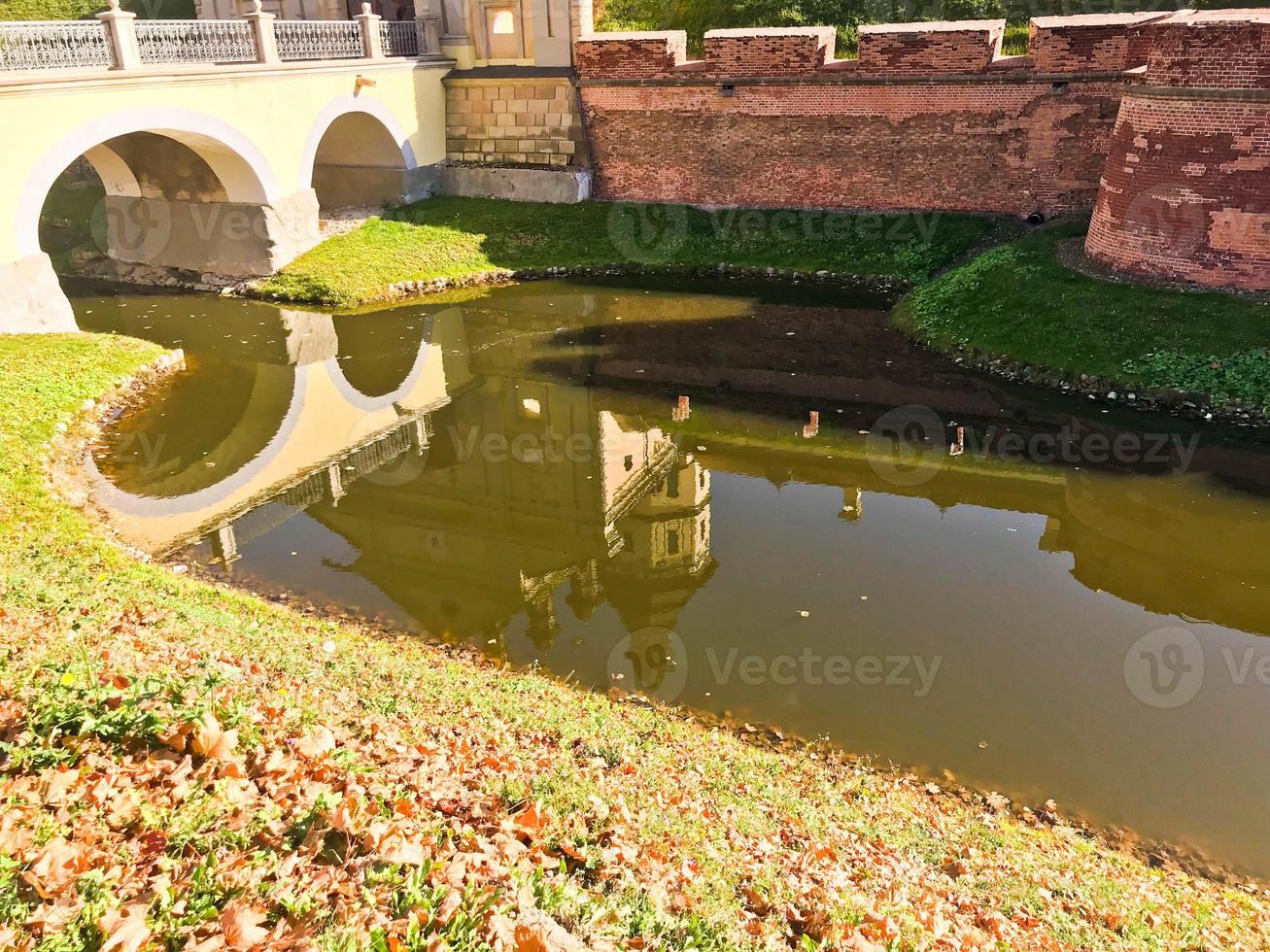 Eine große Erdmauer aus rotem Backstein ist stark schützend und ein Wassergraben mit dem Krieg einer alten, alten mittelalterlichen Burg in der Mitte Europas und ein Fluss mit Wasser foto