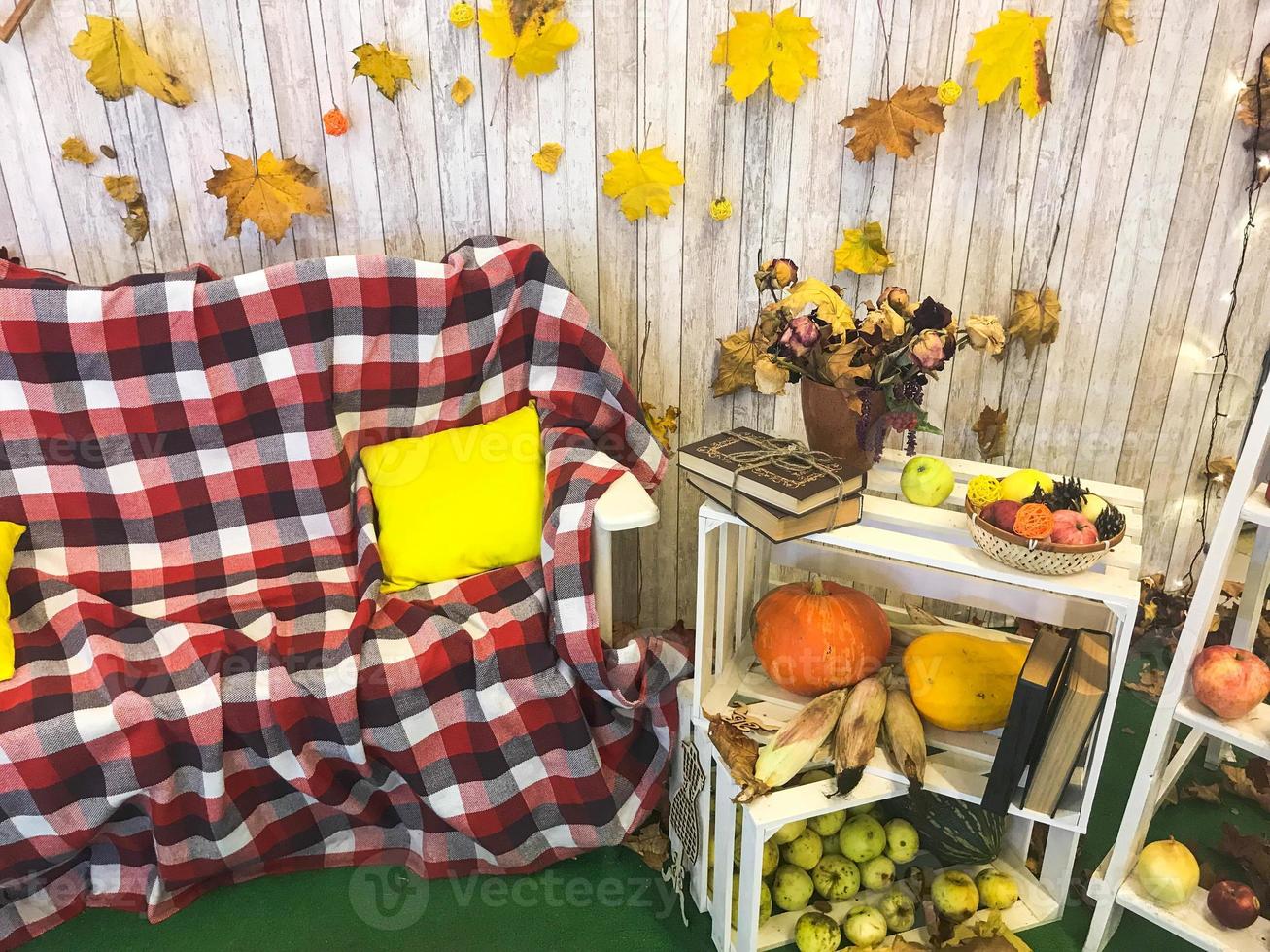 kariertes Plaid auf einem Sessel und einem Holztisch mit Vintage-Büchern, die mit Bindfäden und einer Vase gebunden sind, Herbarium, grüner Apfel auf dem Hintergrund von Holzbrettern und gelben Herbstblättern foto