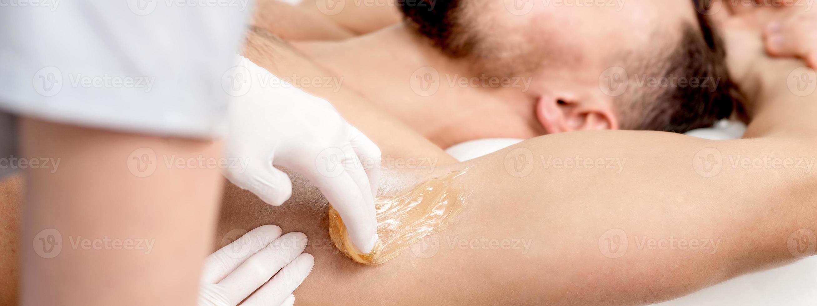 kosmetologe, der wachspaste auf männliche achselhöhle aufträgt foto