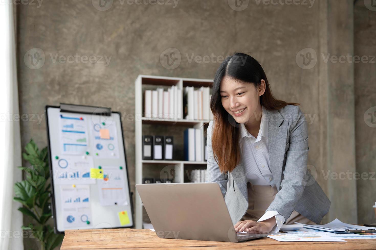 attraktive junge asiatische frau, die laptop-computer verwendet, während sie in einem büro steht. foto