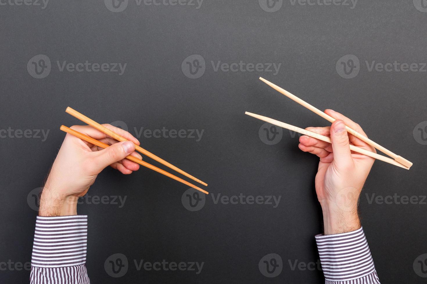 kreatives Bild von Holzstäbchen in zwei männlichen Händen auf schwarzem Hintergrund. japanisches und chinesisches essen mit kopierraum foto