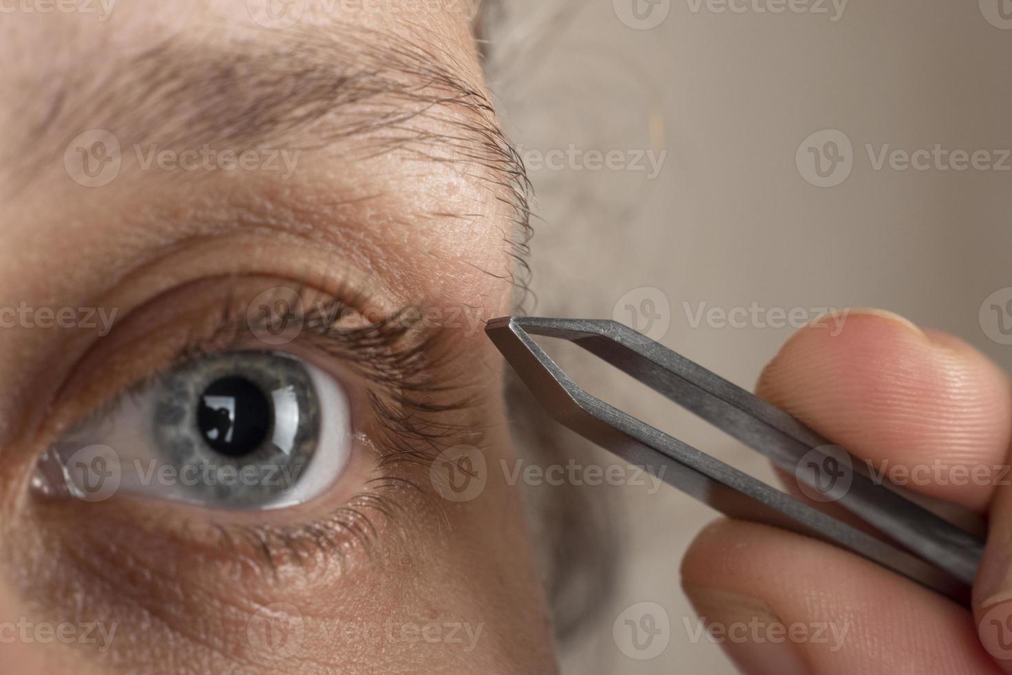 Frau, die mit einer Pinzette Augenbrauenhaare zupft foto