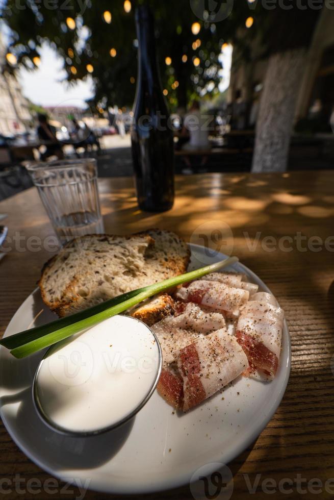 Nahaufnahme Scheiben von geräuchertem Speckfleisch mit Roggenvollkornschwarzbrot, Frühlingszwiebeln und Sauerrahm auf dem Tisch. foto