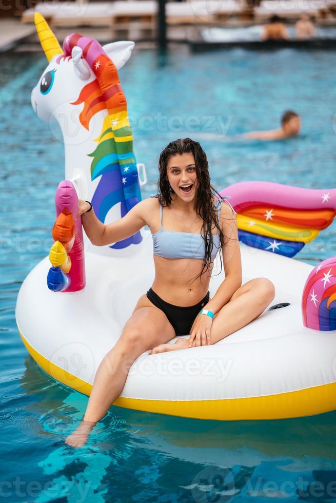 Frau auf aufblasbarer Einhorn-Spielzeugmatratze schwimmt im Pool. foto