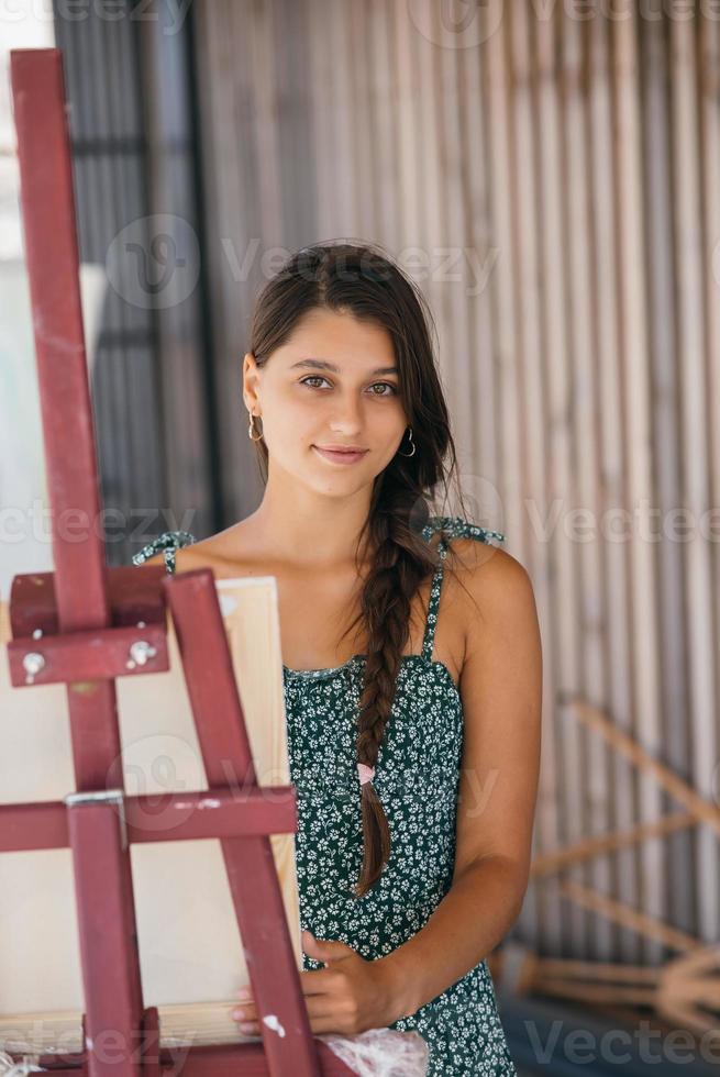 junge schöne künstlerin steht neben einer staffelei mit einer leinwand foto