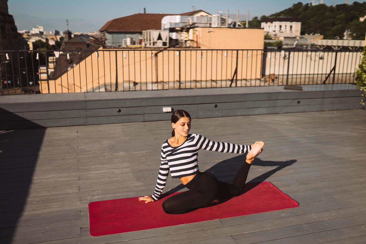 Frau, die am frühen Morgen Yoga-Übungen auf dem Hausdach macht foto
