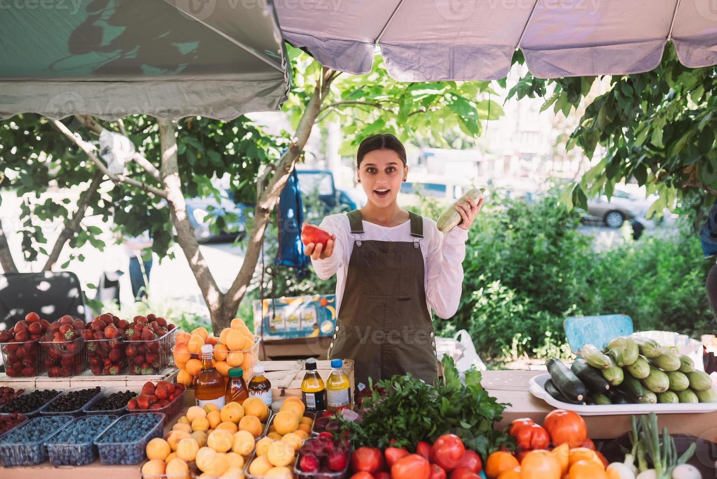 junge Verkäuferin, die Zucchini und Tomate in den Händen hält foto