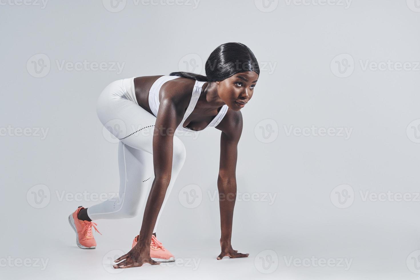 schöne junge Afrikanerin, die in Startposition und vor grauem Hintergrund steht foto