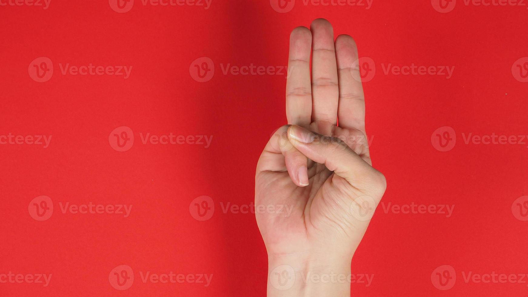 Ein Handzeichen von 3 Fingern zeigt nach oben und bedeutet drei, dritte oder Verwendung aus Protest. Es wird auf roten Hintergrund gesetzt foto