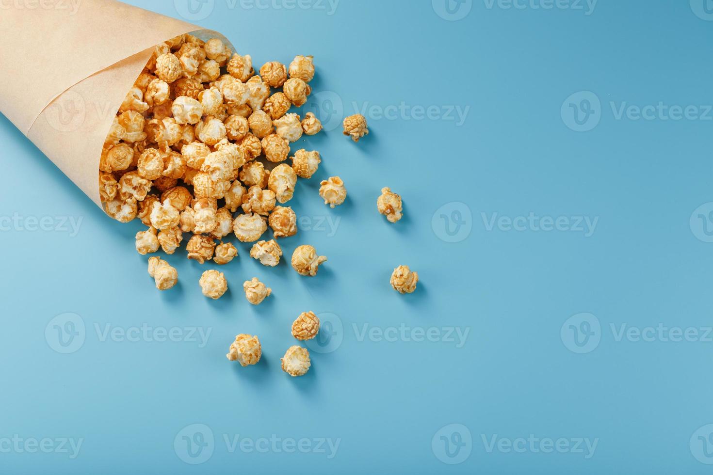 Popcorn in Karamellglasur in einem Papierumschlag auf blauem Hintergrund. foto