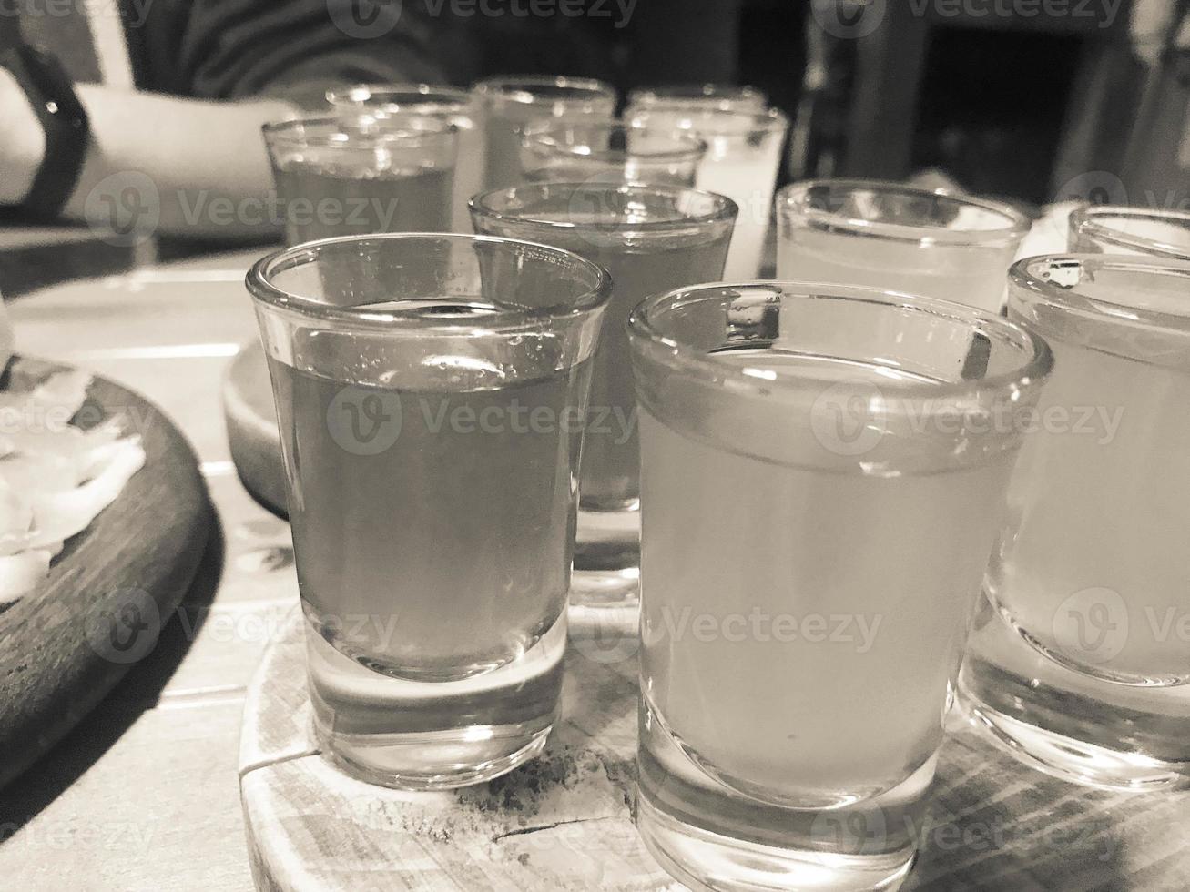 eine reihe von vielen köstlichen schwarz-weiß-gläsern, schüssen mit starkem alkohol, wodka, füllung, brandy auf holzständern auf einem tisch in einem café, einer bar, einem restaurant foto