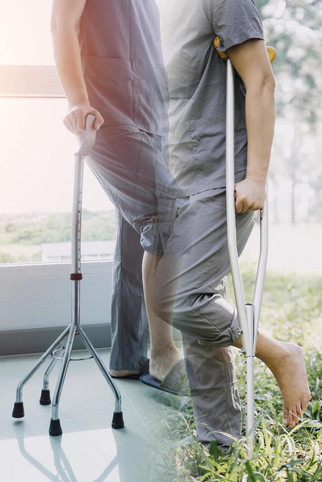 junge asiatische physiotherapeutin, die mit einer älteren frau beim gehen mit einer gehhilfe arbeitet foto