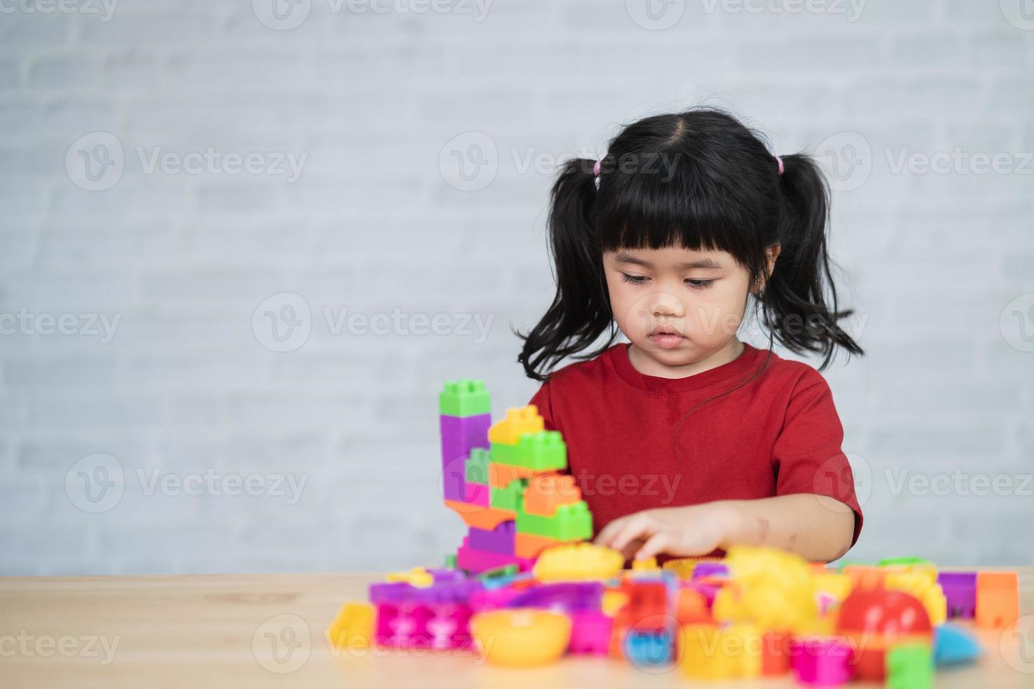 asiatisches süßes lustiges vorschulkind kleines mädchen in einem bunten hemd, das mit lego oder bauspielzeugblöcken spielt, die einen turm im kindergartenzimmer oder im wohnzimmer bauen. Kinder spielen. Kinder in der Tagespflege. foto