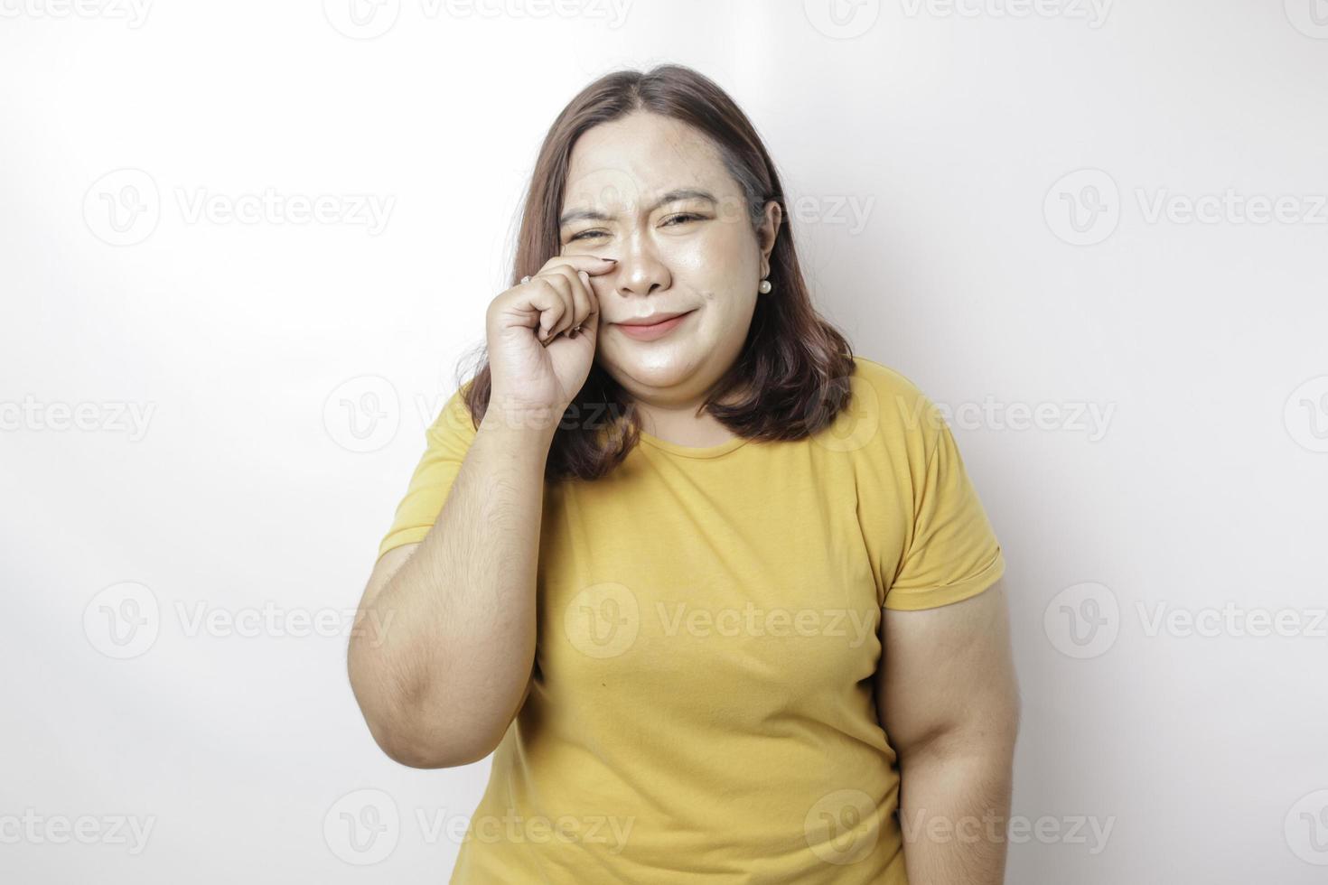 Ein Porträt einer großen asiatischen Frau, die ein gelbes T-Shirt trägt, das von weißem Hintergrund isoliert ist, sieht deprimiert aus foto