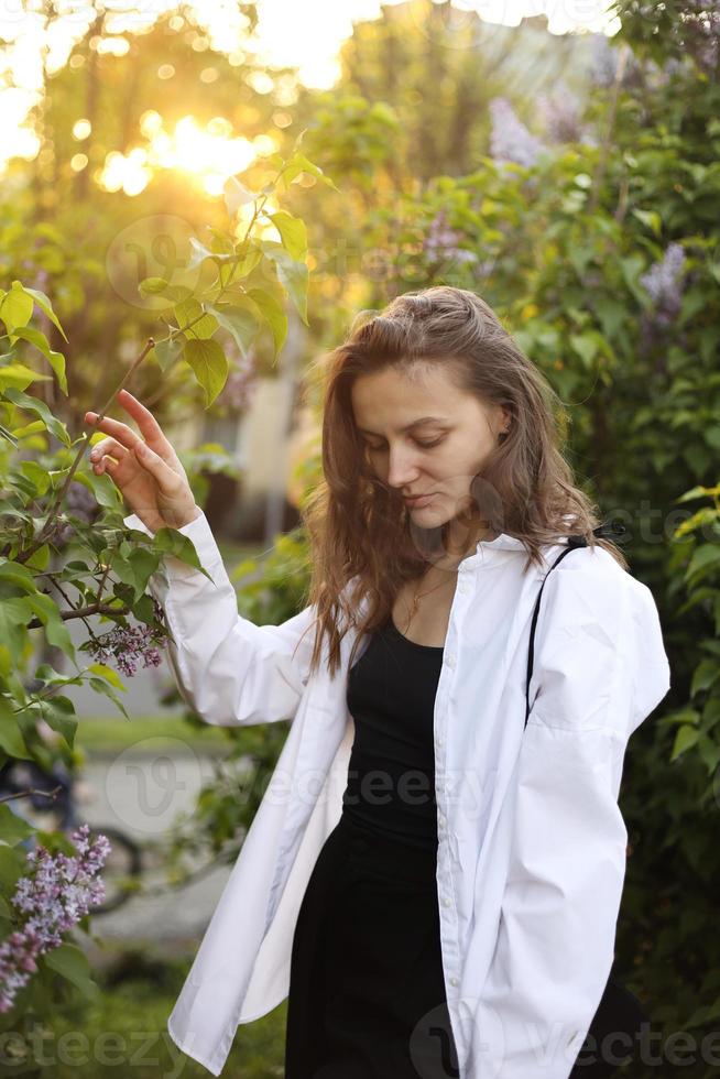 unwirklich atemberaubende schöne junge Frau, die in einem grün blühenden Frühlingsgarten in einem Lavendelgarten mit einem Fliederstrauß in den Händen spazieren geht. romantisches Portrait der Nahaufnahmemode. die Blumen riechen foto