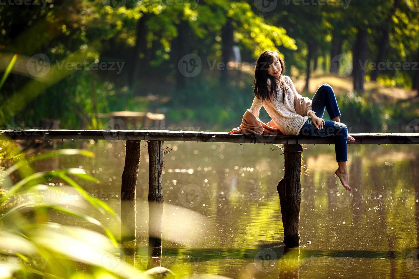 schönes Mädchen mit langen brünetten Haaren, das auf der Brücke sitzt. Natur foto