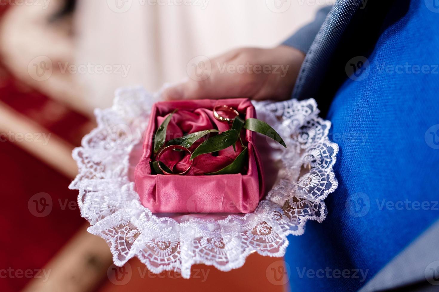 Der Bräutigam hält morgens am Hochzeitstag goldene Eheringe in einer dekorativen Schachtel mit einem grünen und roten Tuch für die Braut. hochwertiges Foto