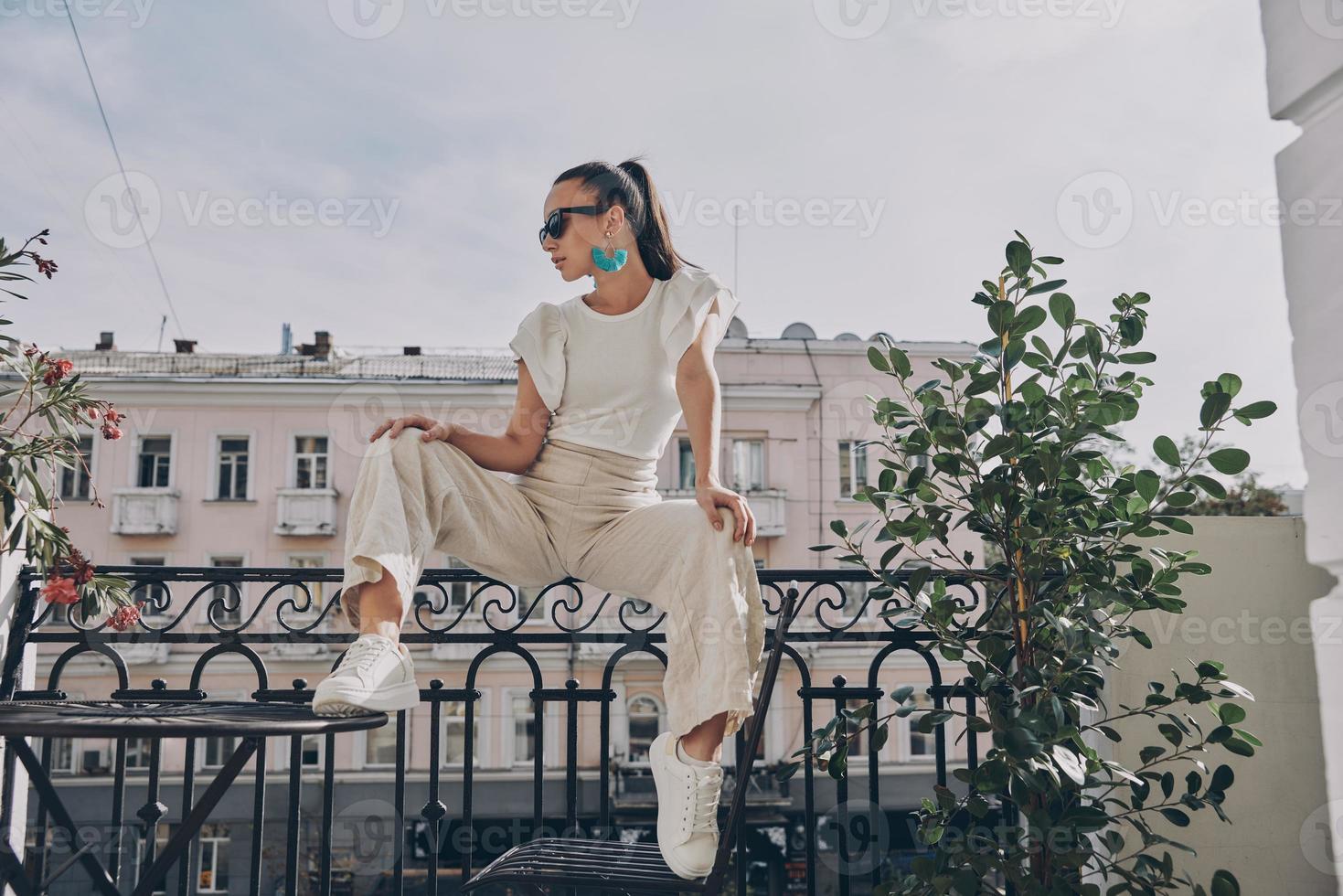 modische junge frau mit brille, die auf dem balkon sitzt foto