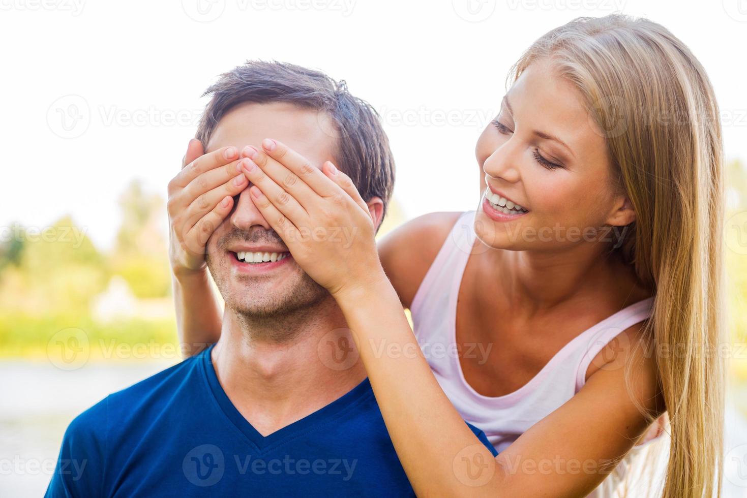 Ratet mal, wer die schöne junge Frau, die die Augen ihres Freundes bedeckt und lächelt, während beide draußen stehen foto