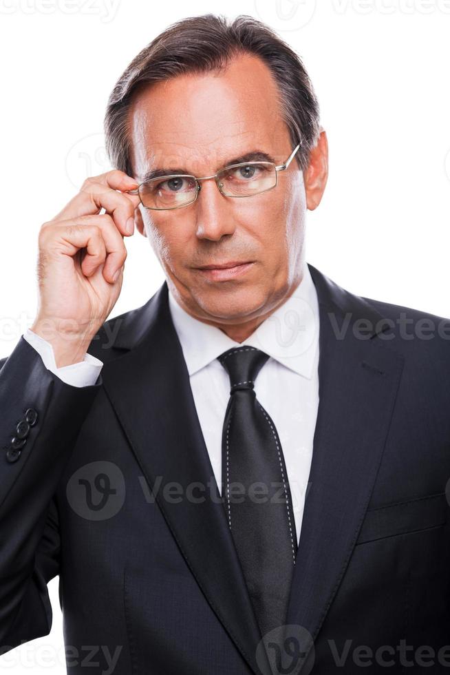 Wie kann ich Ihnen helfen? Porträt eines selbstbewussten reifen Mannes in Abendkleidung, der seine Brille anpasst und in die Kamera schaut, während er vor weißem Hintergrund steht foto