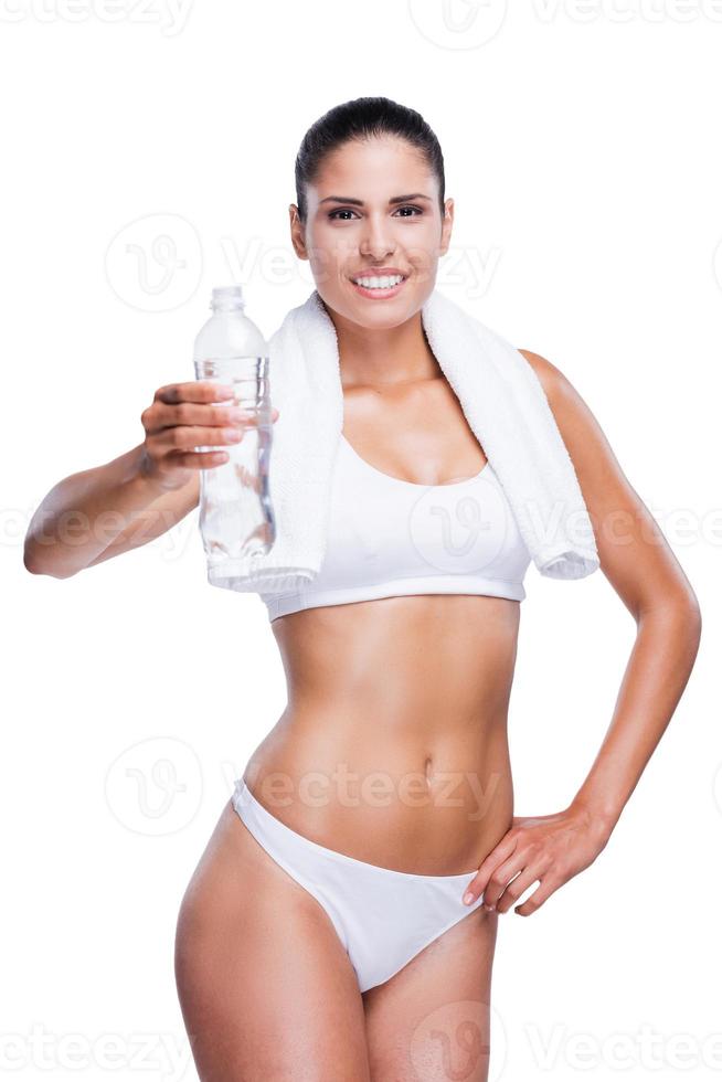 Bleiben Sie hydratisiert Schöne junge Frau in weißem BH und Höschen, die eine Flasche mit Wasser hält und lächelt, während sie isoliert auf Weiß steht foto