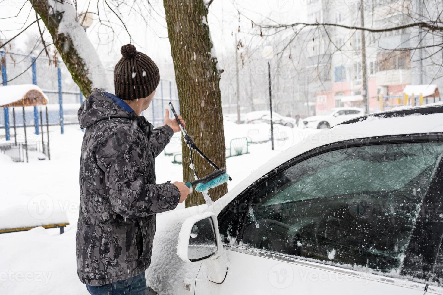 Ein Mann wischt nach einem Schneefall Schnee von einem Auto. eine hand in einer  blauen jacke mit einem autobesen auf dem weißen körper. winterliche  Wetterlage 9966987 Stock-Photo bei Vecteezy