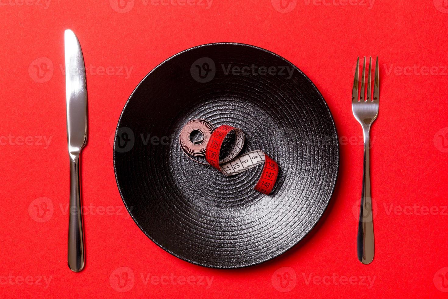 gesundes Ernährungskonzept der Platte mit Maßband, Gabel und Messer auf rotem Hintergrund. Ansicht von oben foto
