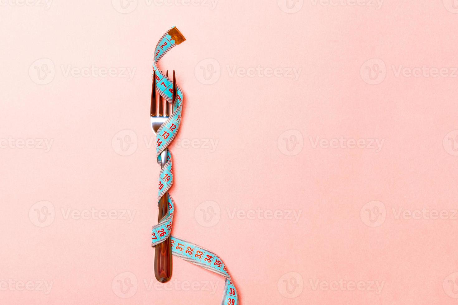 Nahaufnahme der Gabel in Maßband auf rosa Hintergrund gewickelt. Konzept für Übergewicht und Überernährung foto
