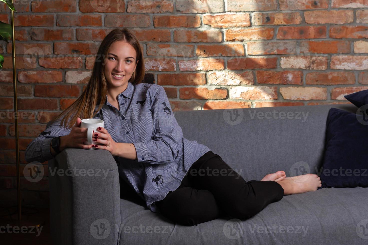 lächelnde Frau auf der Couch mit weißer Tasse foto