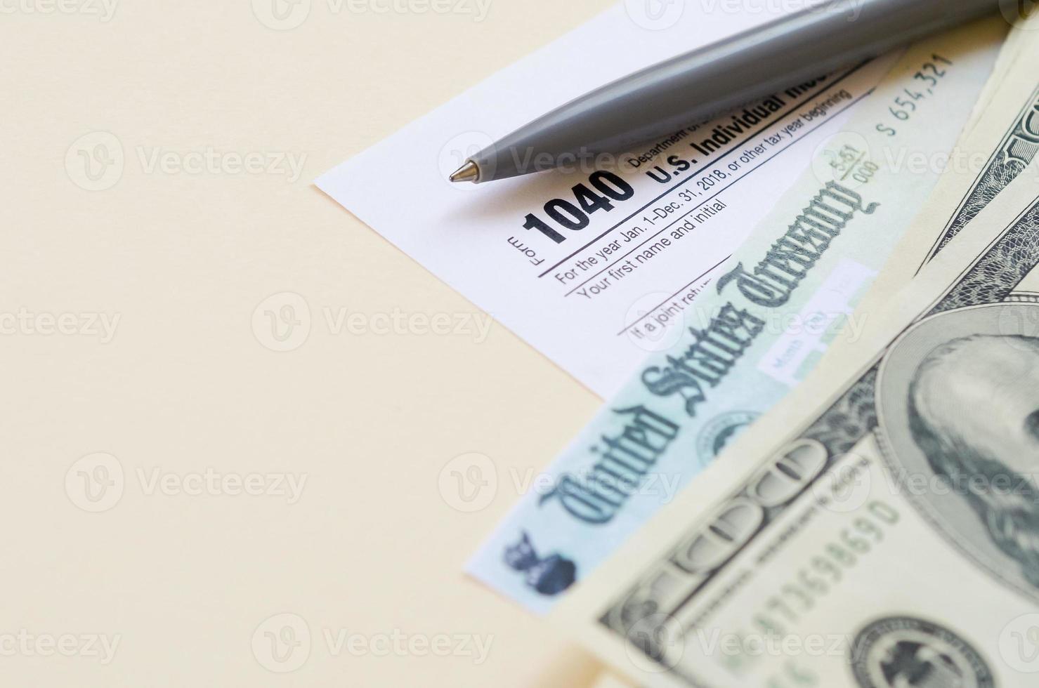 1040 individuelles Einkommensteuererklärungsformular mit Rückerstattungsscheck und Hundert-Dollar-Scheinen auf beigem Hintergrund foto