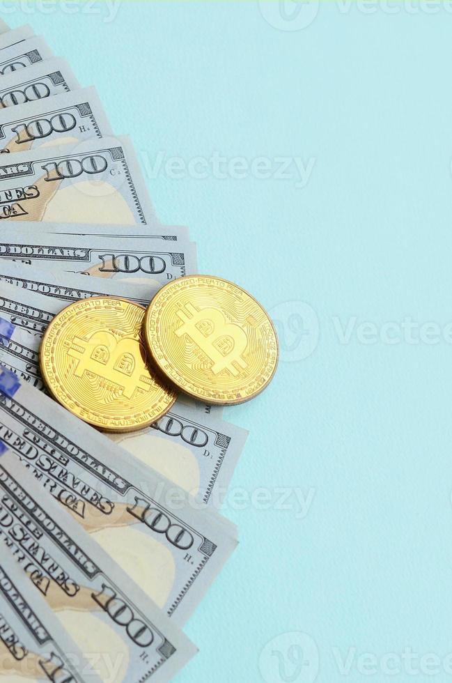 goldene bitcoins und hundertdollarscheine liegen auf hellblauem hintergrund foto