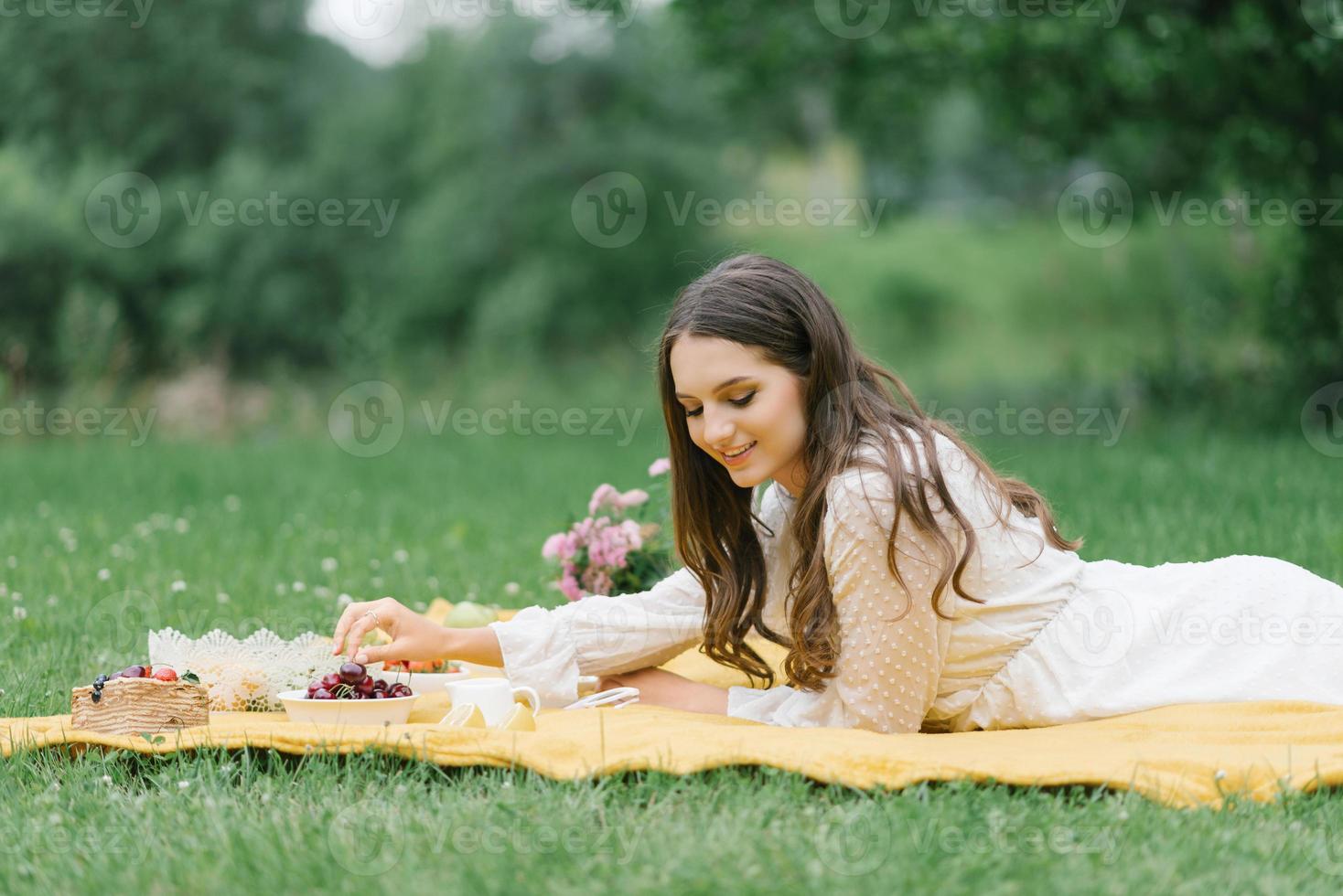 lächelndes kaukasisches jugendlich Mädchen, das draußen sitzt. kreative künstlerische junge frau, die lässige kleidung trägt und am sommertag ein picknick mit früchten hat. foto