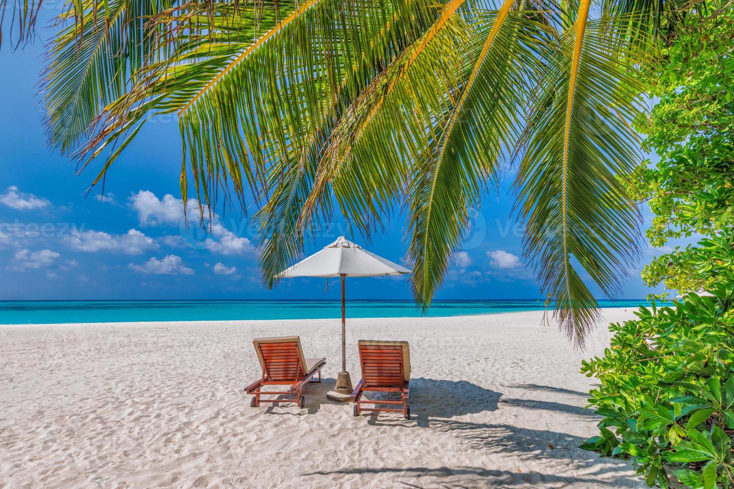 schöne tropische sonnige küste, paar sonnenliegen oder stühle regenschirm unter palmenblättern. Meer Sand Horizont Himmel. romantischer Relax-Lifestyle inspiriert den Hintergrund des Inselstrandes. sommerreise exotischer urlaub foto