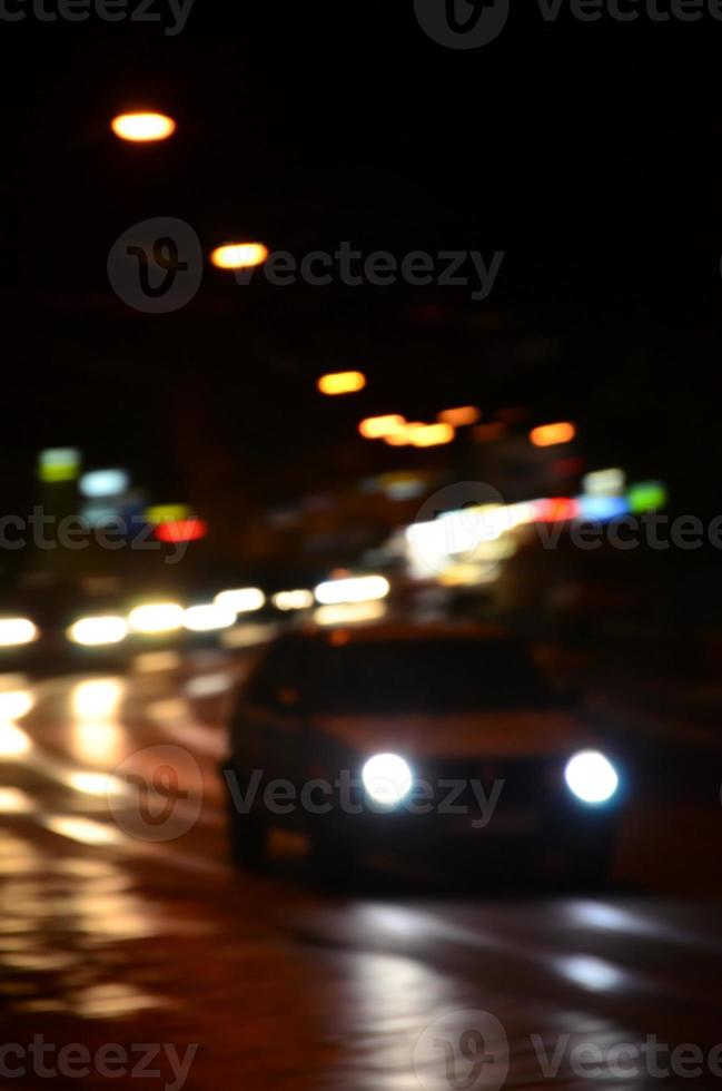 verschwommene Nachtszene des Verkehrs auf der Fahrbahn. defokussiertes Bild von Autos, die mit leuchtenden Scheinwerfern fahren. Bokeh-Kunst foto