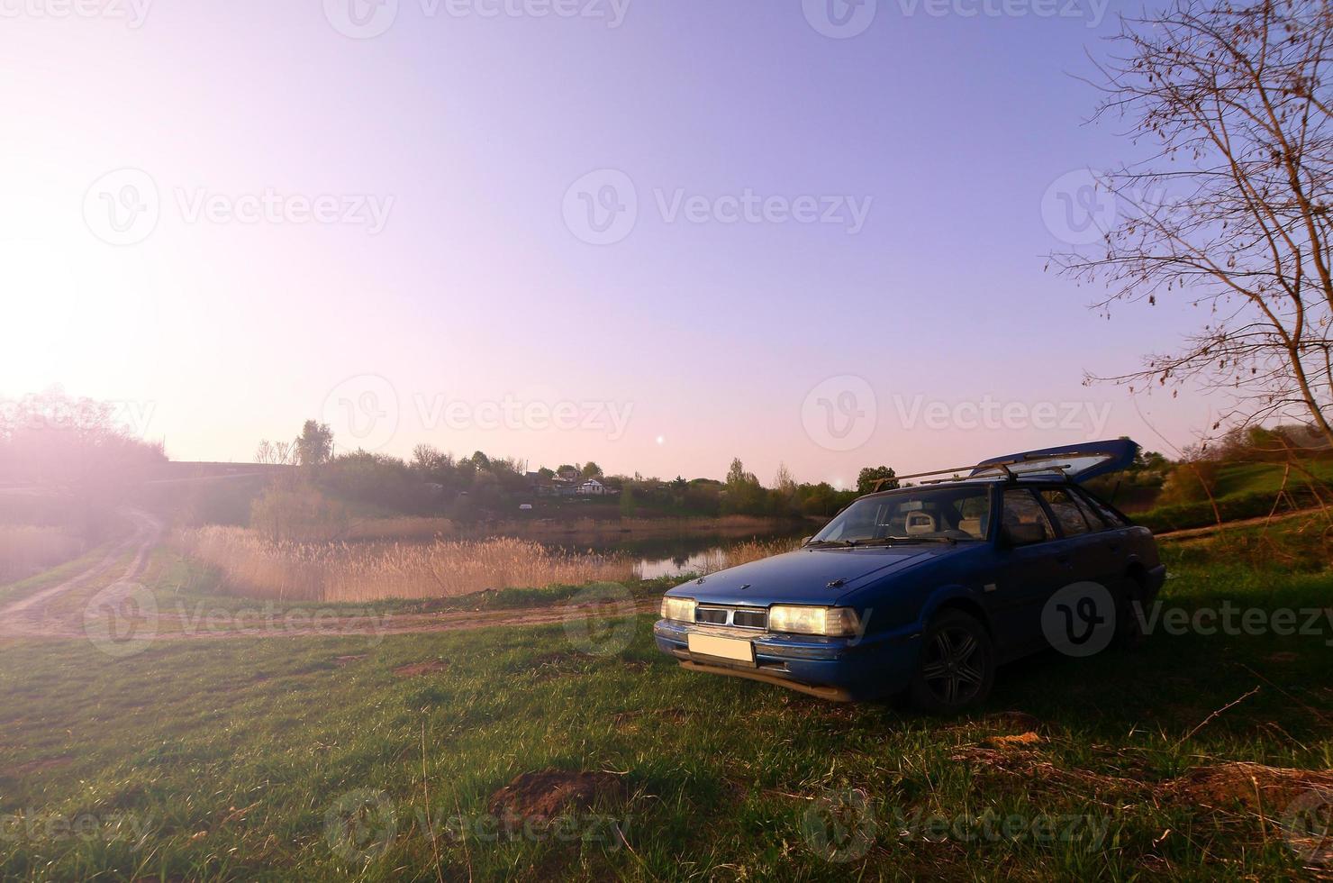 Ein blaues Auto vor dem Hintergrund einer rustikalen Landschaft mit einem wilden Zuckerrohrfeld und einem kleinen See. Die Familie kam in der Natur in der Nähe des Sees zur Ruhe foto