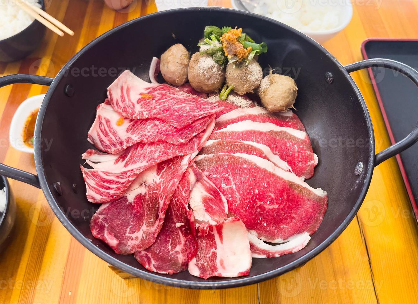frische Rindfleischscheibe in der Pfanne mit Fleischbällchen und etwas Gemüse servieren, bevor die heiße Suppe gefüllt wird foto