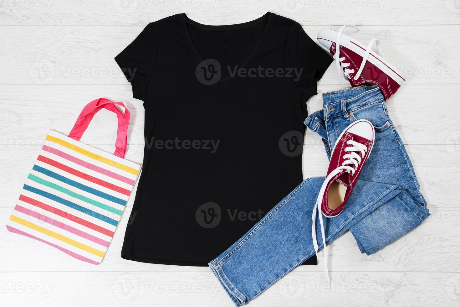 T-Shirt schwarz und Turnschuhe. t-shirt-modell flach lag mit sommeraccessoires. Jeans und Turnschuhe auf Holzbodenhintergrund. Platz kopieren. Vorlage leere Leinwand. Vorderansicht von oben. foto