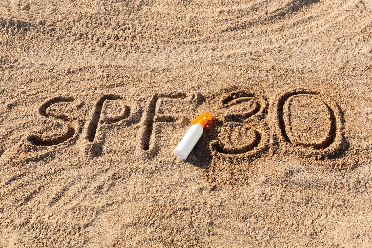 Sonnenschutzfaktor dreißig. spf 30 wort geschrieben auf dem sand und der weißen flasche mit sonnencreme. hintergrund des hautpflegekonzepts foto