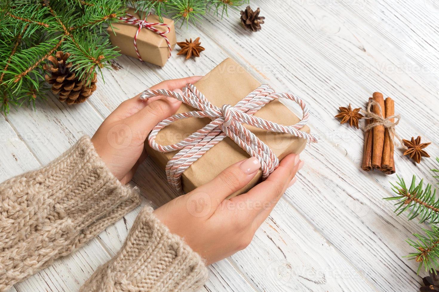 weibliche hände, die handgefertigte geschenkbox aus recyceltem papier auf weißem holztischhintergrund halten. weihnachtsvorbereitungskonzept, geschenkverpackungshintergrund foto