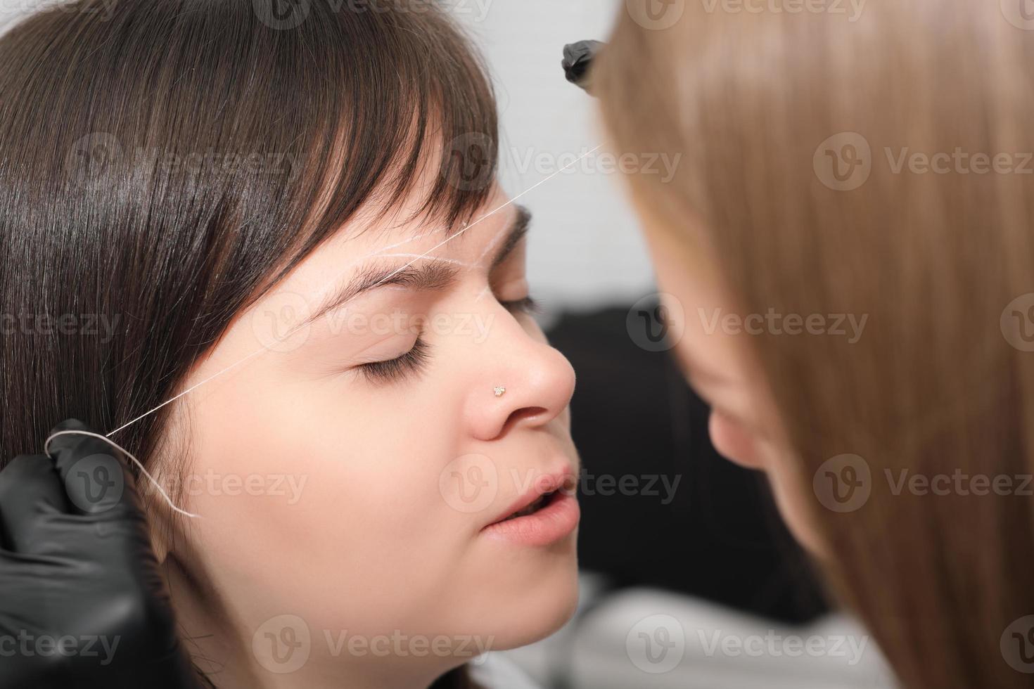 Kundin mit geschlossenen Augen im Schönheitssalon während des Stirnkorrekturverfahrens. Markierungen im Gesicht der Frau machen, um Permanent Make-up zu machen. foto