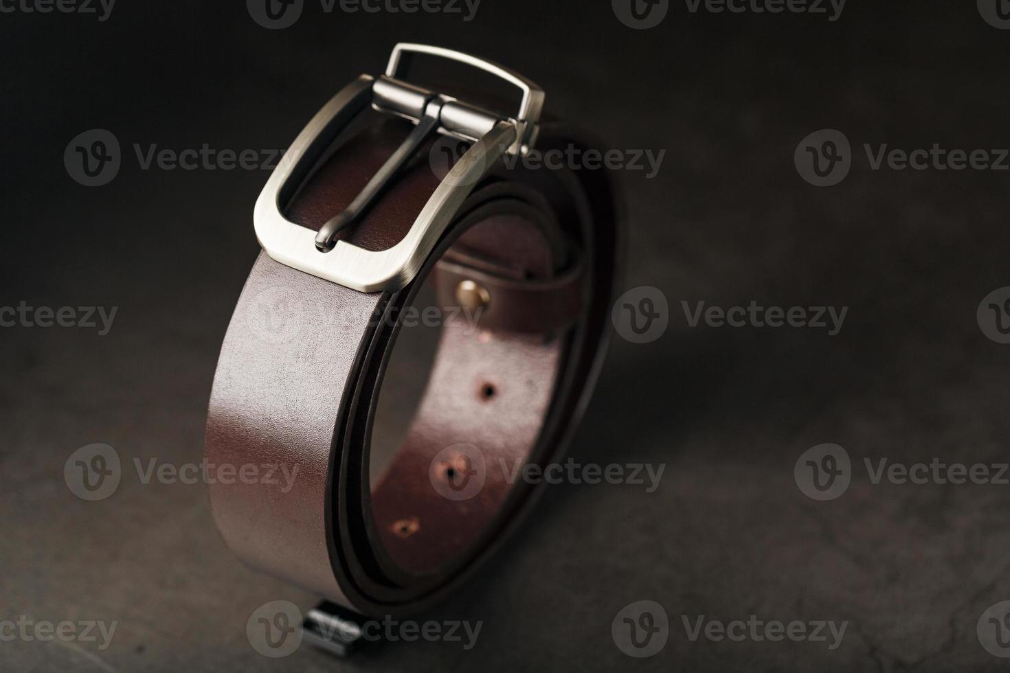 modischer brauner Herrengürtel aus echtem Leder mit heller Metallschnalle auf dunklem Grund. echtes Leder, handgefertigt foto
