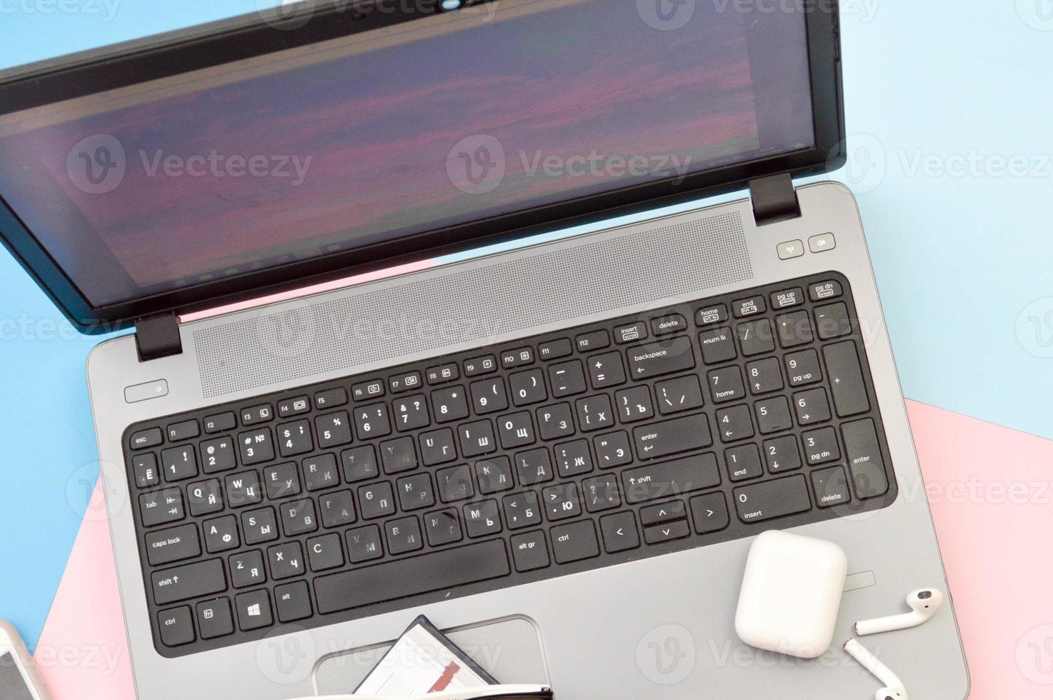 Arbeitsplatz zu Hause, Heimbüro für Fernarbeit mit einem Computer Laptop Handy Smartphone Notizblock Stift Kopfhörer und Brille auf rosa und blauem Hintergrund foto